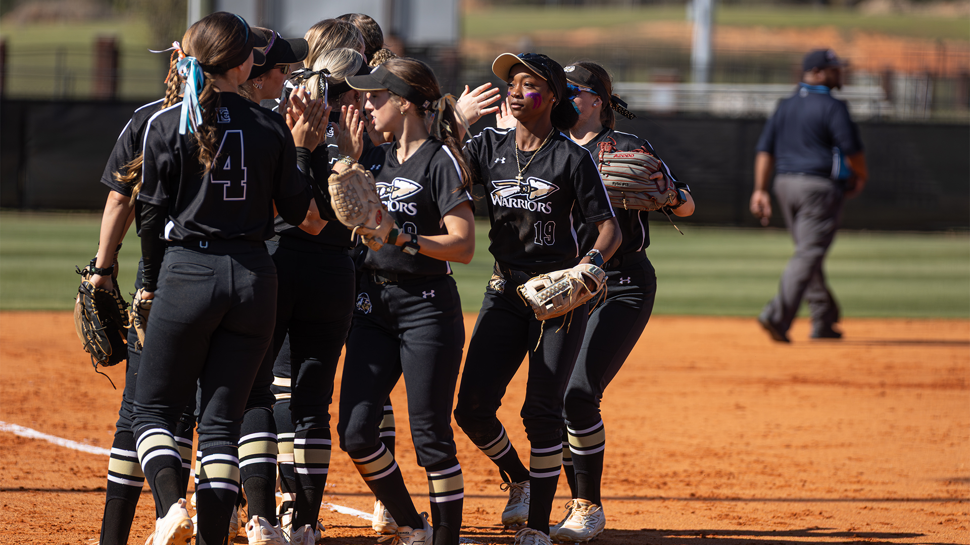 Softball girls in black warrior jersey's in a huddle high fiving each other